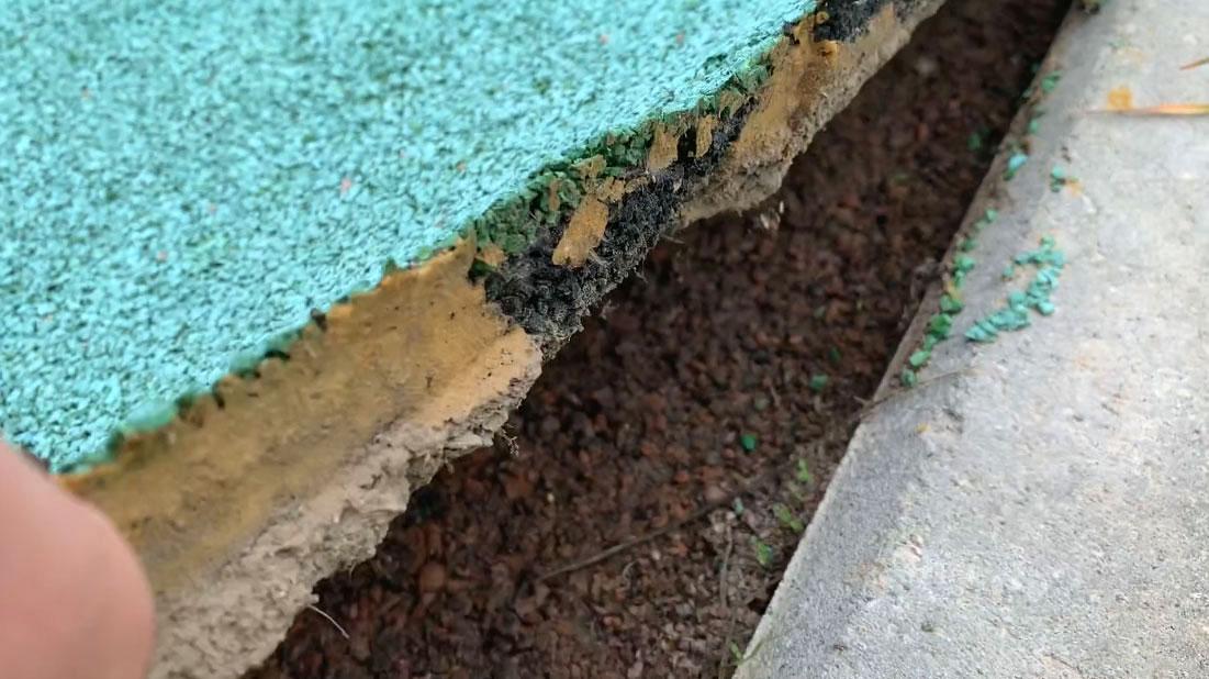 Фрагмент резинового покрытия спортивной площадки у бортового камня с раскрытой кромкой и видимыми слоями