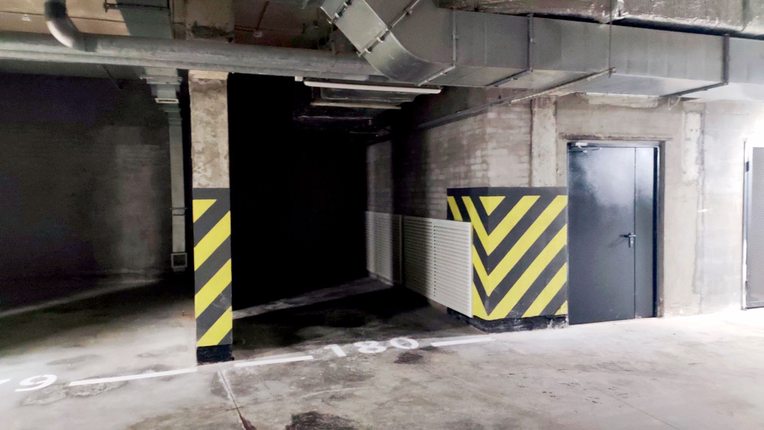 Машино-место в подземном паркинге, зауженное кирпичной стеной и вентиляционным коробом