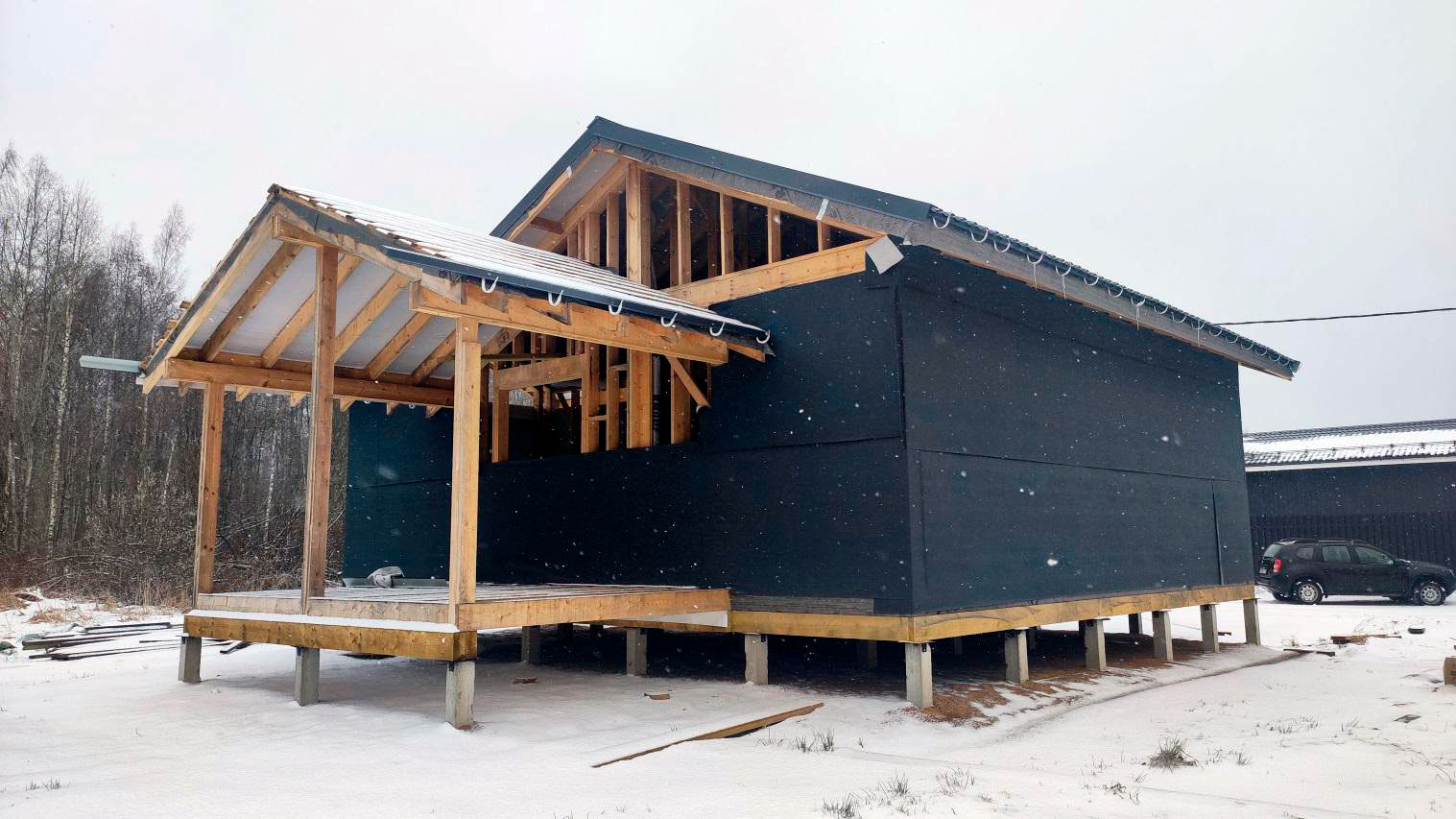 Недостроенный каркасный дом на железобетонных сваях зимой: вид снаружи, частично обшитые стены и открытые элементы каркаса