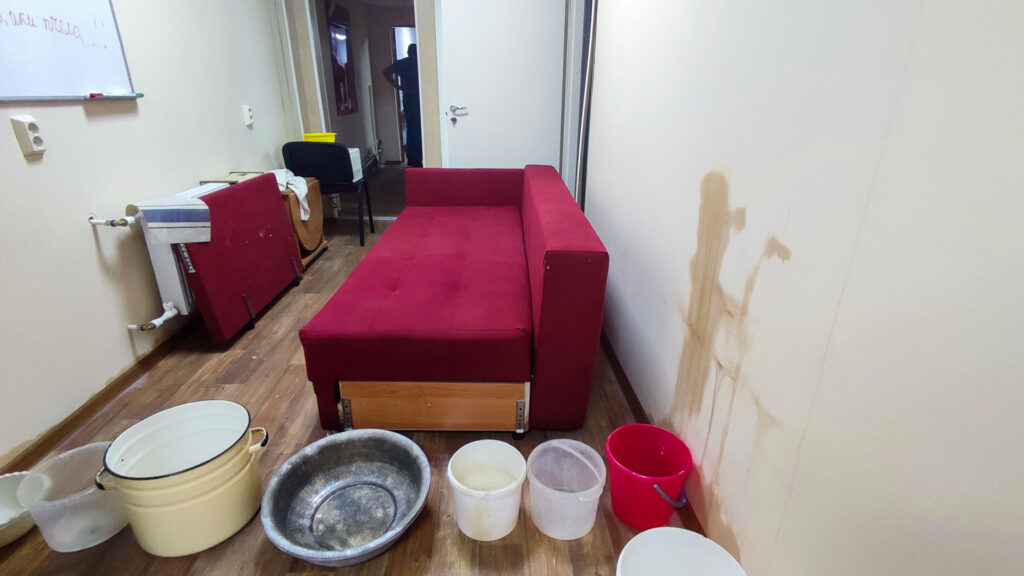 Залив квартиры: следы протечки на стене и емкости для сбора воды в комнате