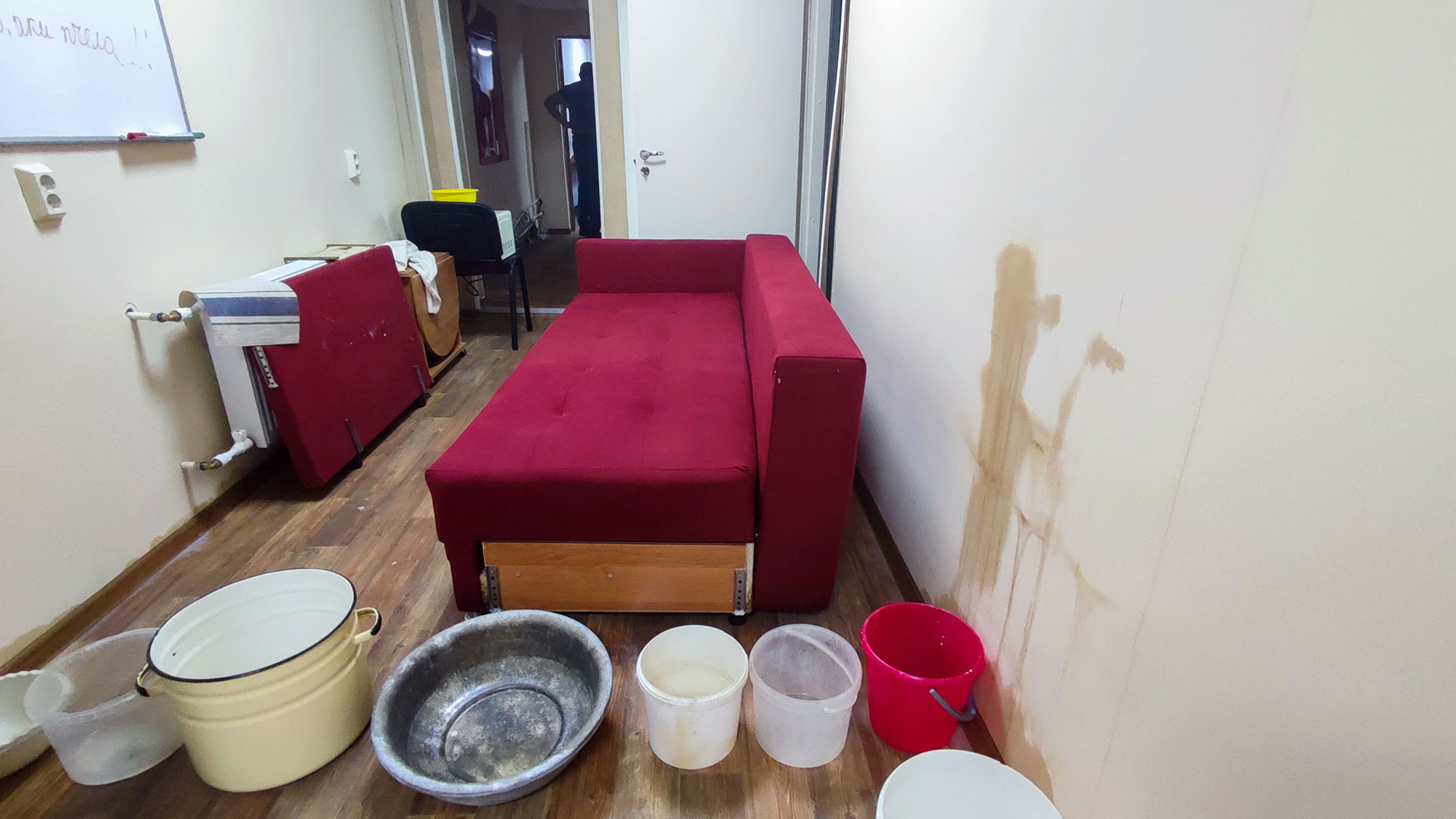 Залив квартиры: следы протечки на стене и емкости для сбора воды в комнате